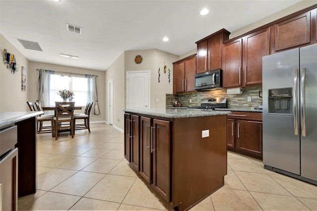 2319 Dammar St, Orlando, FL 32824 - kitchen featuring appliances with stainless steel finishes, light tile patterned floors, backsplash, a center island, and light stone countertops