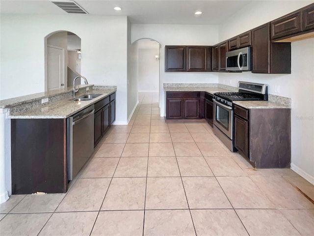 10429 Avelar Ridge Dr, Riverview, FL 33578 - kitchen featuring appliances with stainless steel finishes, arched walkways, dark brown cabinets, light stone counters, and recessed lighting