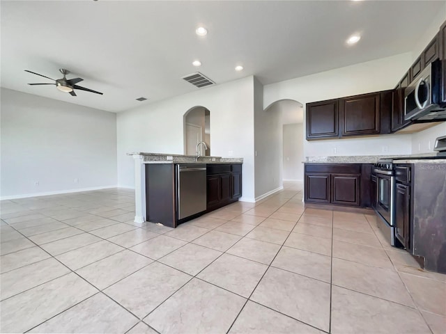 10429 Avelar Ridge Dr, Riverview, FL 33578 - kitchen with stainless steel appliances, arched walkways, light tile patterned floors, dark brown cabinetry, and recessed lighting
