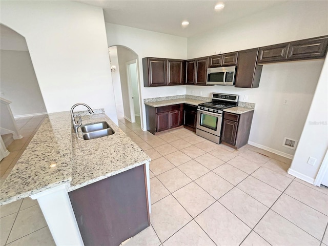 10429 Avelar Ridge Dr, Riverview, FL 33578 - kitchen with appliances with stainless steel finishes, a peninsula, light stone countertops, arched walkways, and dark brown cabinetry