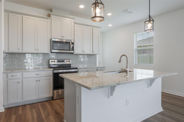 3240 Canna Lily Pl, Clermont, FL 34711 - kitchen with appliances with stainless steel finishes, dark wood-style flooring, an island with sink, tasteful backsplash, and white cabinetry