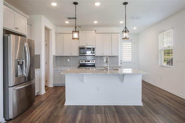 3240 Canna Lily Pl, Clermont, FL 34711 - kitchen with stainless steel appliances, decorative backsplash, dark wood-style flooring, an island with sink, and white cabinets