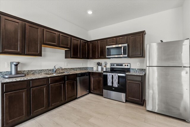 827 Grandin St, Davenport, FL 33837 - kitchen featuring appliances with stainless steel finishes, light stone countertops, dark brown cabinetry, light wood finished floors, and recessed lighting