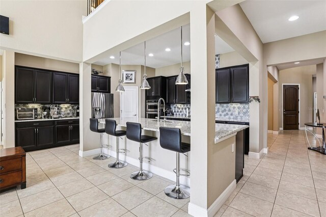 9207 Busaco Park Way, Winter Garden, FL 34787 - kitchen featuring light tile patterned flooring, dark cabinetry, decorative backsplash, light stone countertops, and a kitchen bar