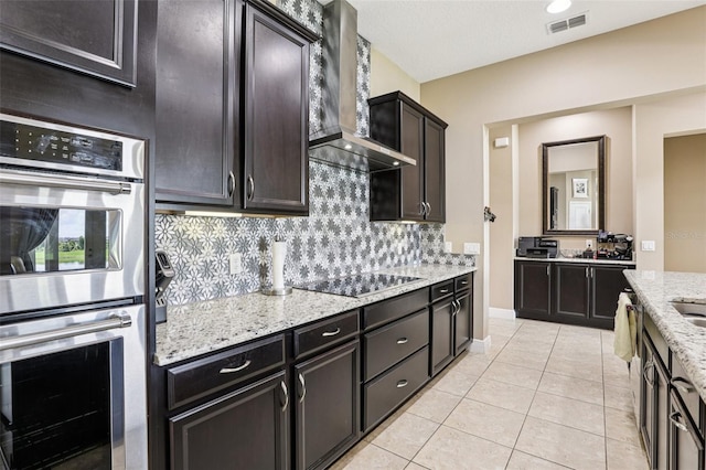 9207 Busaco Park Way, Winter Garden, FL 34787 - kitchen featuring wall chimney range hood, stainless steel double oven, black electric cooktop, tasteful backsplash, and light stone counters