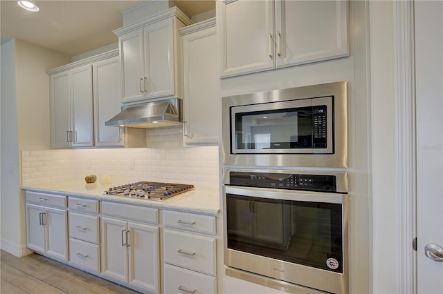 1774 Pasture Loop, Oviedo, FL 32765 - kitchen featuring appliances with stainless steel finishes, under cabinet range hood, backsplash, white cabinetry, and light wood-style floors