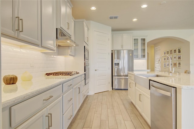 1774 Pasture Loop, Oviedo, FL 32765 - kitchen featuring appliances with stainless steel finishes, under cabinet range hood, arched walkways, light wood finished floors, and tasteful backsplash