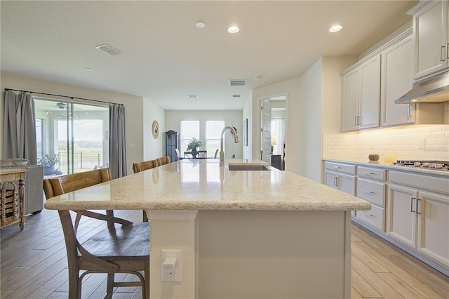 1774 Pasture Loop, Oviedo, FL 32765 - kitchen with stainless steel gas cooktop, a kitchen island with sink, light wood finished floors, tasteful backsplash, and white cabinetry