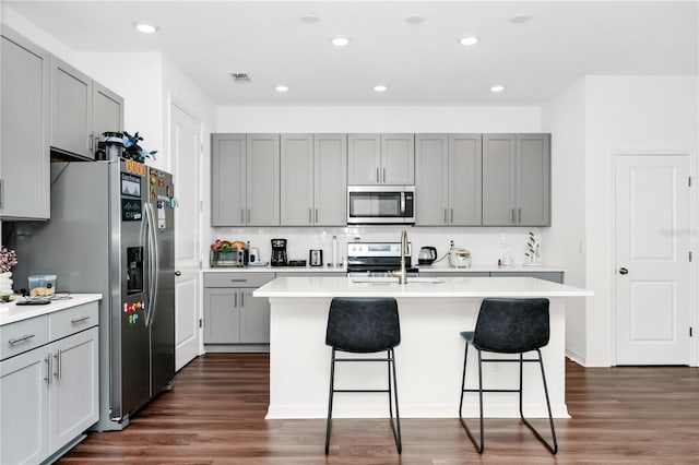 812 Benoi Dr, Davenport, FL 33896 - kitchen with appliances with stainless steel finishes, gray cabinetry, a breakfast bar area, a kitchen island with sink, and light countertops