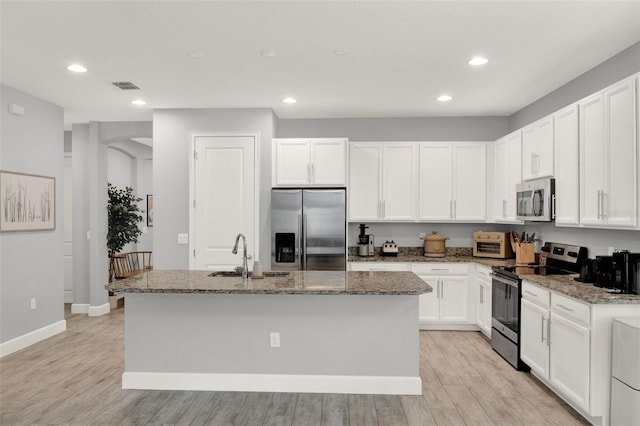 1061 Castlevecchio Loop, Orlando, FL 32825 - kitchen featuring appliances with stainless steel finishes, recessed lighting, white cabinets, dark stone countertops, and an island with sink
