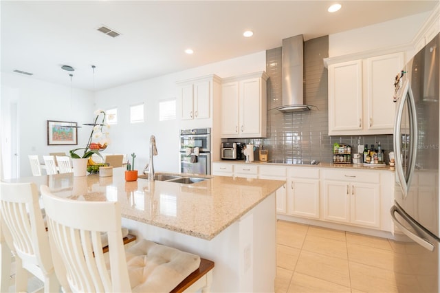 1545 Fairview Cir, Reunion, FL 34747 - kitchen with stainless steel appliances, wall chimney range hood, decorative backsplash, a breakfast bar area, and white cabinetry