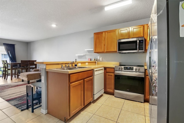 509 Cresting Oak Cir Unit 73, Orlando, FL 32824 - kitchen with appliances with stainless steel finishes, a peninsula, a textured ceiling, light tile patterned floors, and brown cabinetry