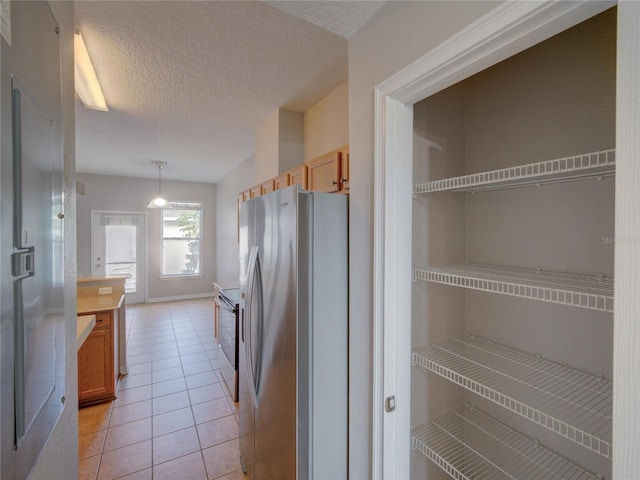 7462 Bentonshire Ave, Windermere, FL 34786 - kitchen featuring appliances with stainless steel finishes, a textured ceiling, light tile patterned flooring, brown cabinets, and pendant lighting