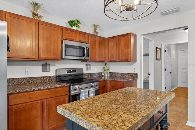 1224 Blackwater Pond Dr, Orlando, FL 32828 - kitchen with appliances with stainless steel finishes, a kitchen island, a textured ceiling, a chandelier, and brown cabinets