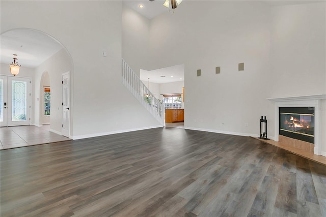 19554 Spring Oak Dr, Eustis, FL 32736 - unfurnished living room featuring a towering ceiling, arched walkways, dark wood-style floors, a fireplace with flush hearth, and stairway
