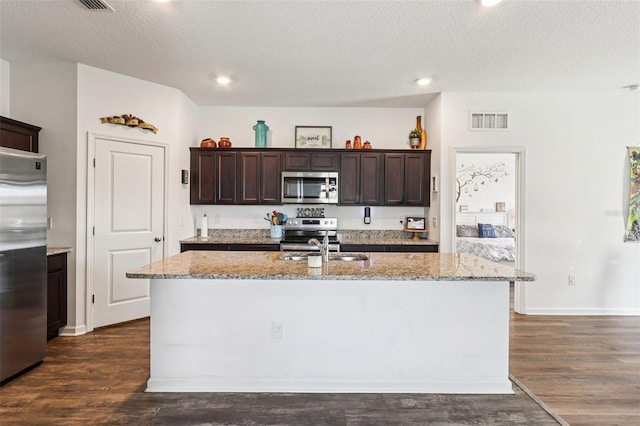 785 Orchid Grove Blvd, Davenport, FL 33837 - kitchen featuring stainless steel appliances, dark brown cabinetry, a center island with sink, light stone countertops, and dark wood finished floors