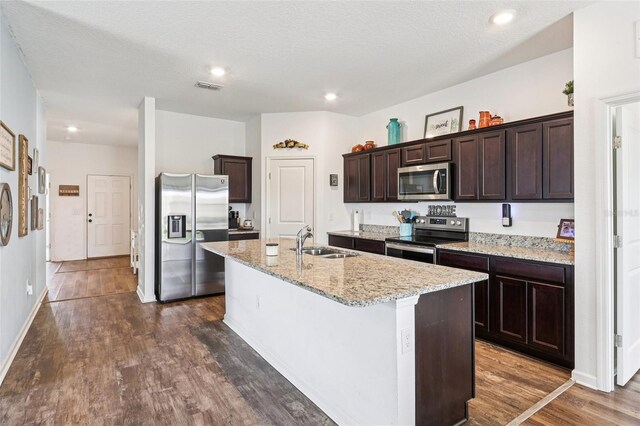 785 Orchid Grove Blvd, Davenport, FL 33837 - kitchen with stainless steel appliances, dark brown cabinetry, dark wood finished floors, a kitchen island with sink, and light stone countertops