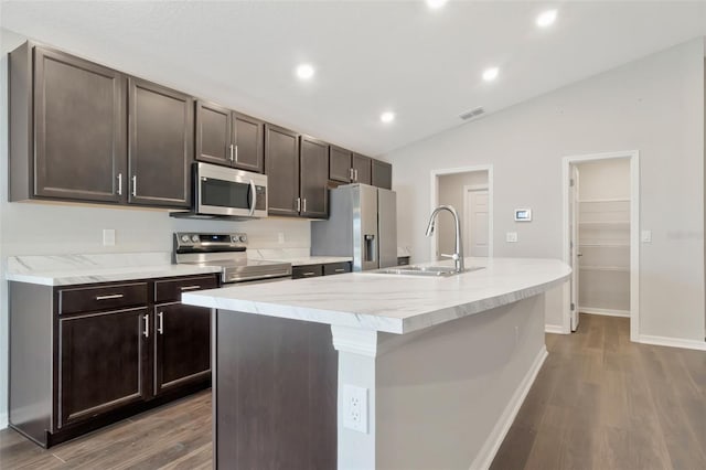 1159 Mountain Flower Ln, Davenport, FL 33837 - kitchen featuring stainless steel appliances, vaulted ceiling, wood finished floors, a kitchen island with sink, and dark brown cabinets