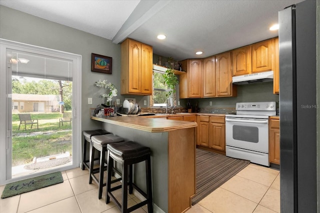 303 Mariana Way, Kissimmee, FL 34758 - kitchen featuring white range with electric stovetop, freestanding refrigerator, a peninsula, under cabinet range hood, and light tile patterned flooring