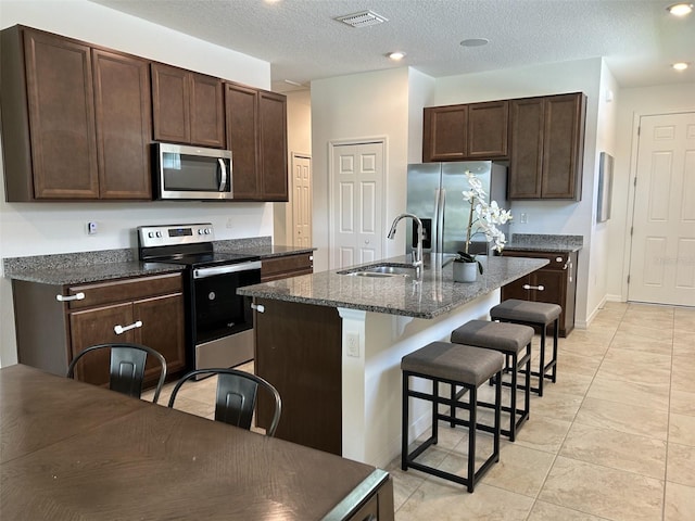 2824 Neverland Dr, New Smyrna Beach, FL 32168 - kitchen with appliances with stainless steel finishes, a breakfast bar, dark brown cabinets, a kitchen island with sink, and recessed lighting