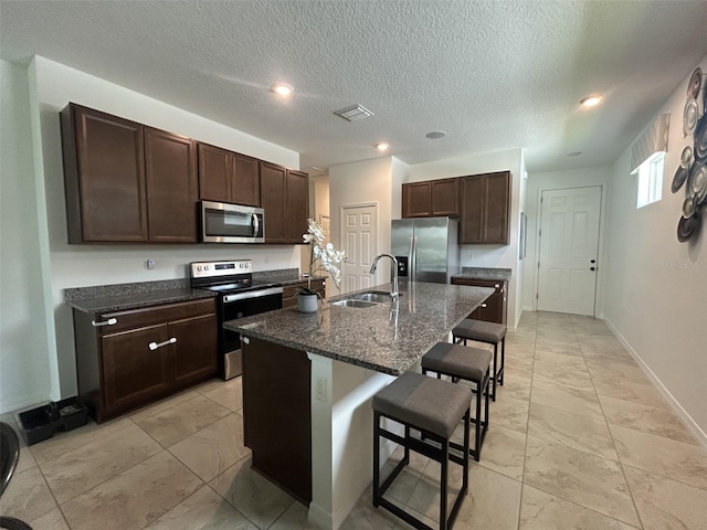 2824 Neverland Dr, New Smyrna Beach, FL 32168 - kitchen featuring appliances with stainless steel finishes, a kitchen breakfast bar, dark brown cabinets, a center island with sink, and light marble finish flooring
