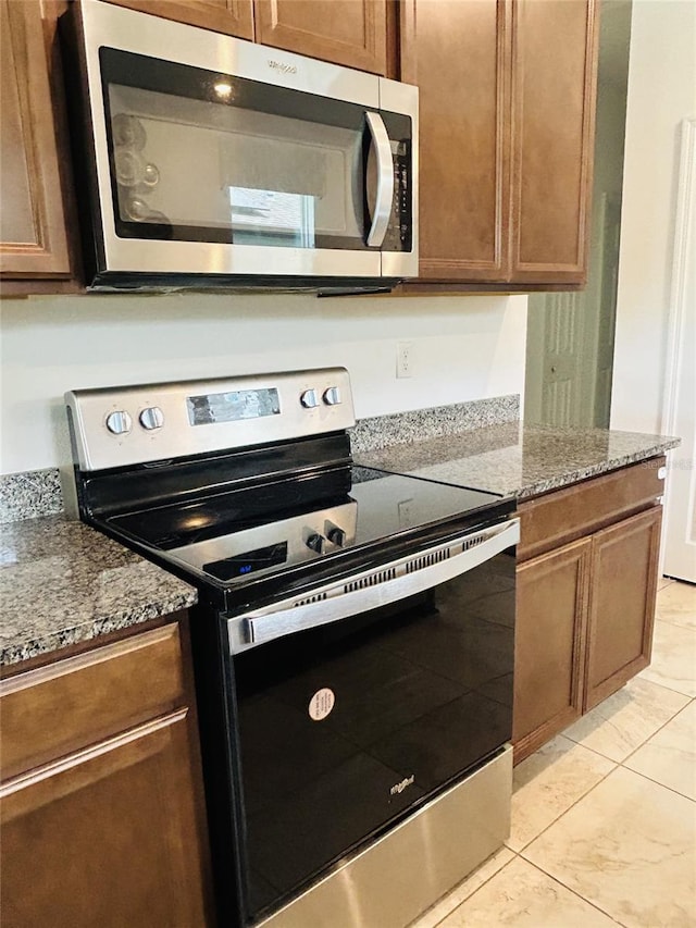 2824 Neverland Dr, New Smyrna Beach, FL 32168 - kitchen with stainless steel appliances, stone counters, light tile patterned floors, and brown cabinetry