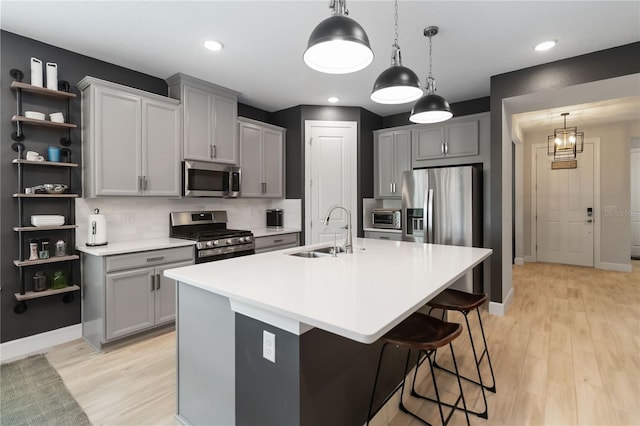 971 Braewood Dr, Clermont, FL 34715 - kitchen with stainless steel appliances, an island with sink, gray cabinetry, light wood finished floors, and decorative light fixtures