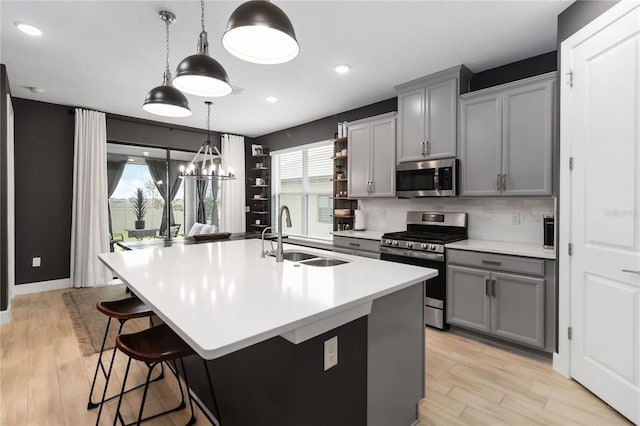 971 Braewood Dr, Clermont, FL 34715 - kitchen featuring appliances with stainless steel finishes, gray cabinetry, a kitchen island with sink, light countertops, and a kitchen bar