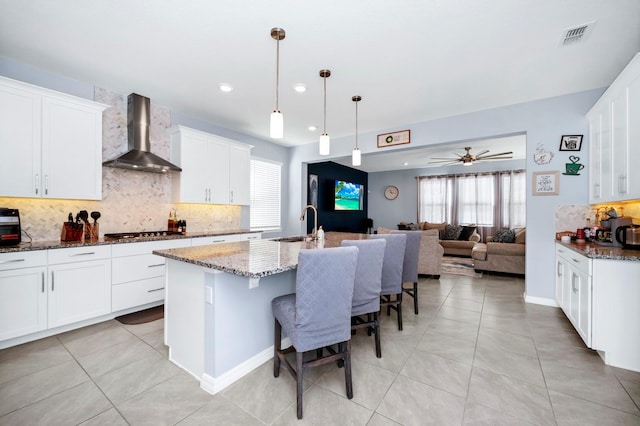 609 Big Pine Ave, Minneola, FL 34715 - kitchen featuring wall chimney range hood, stainless steel gas cooktop, tasteful backsplash, light tile patterned floors, and dark stone counters