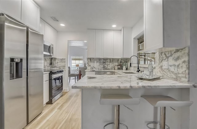 1921 Heathwood Dr, Winter Park, FL 32792 - kitchen featuring appliances with stainless steel finishes, white cabinets, a peninsula, decorative backsplash, and recessed lighting
