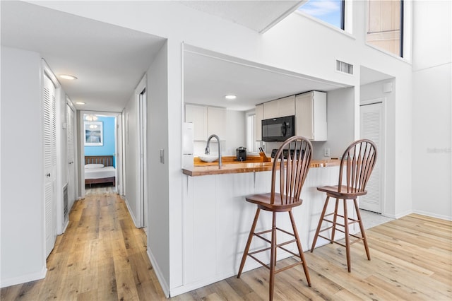 1051 S Highland St Unit 7D, Mount Dora, FL 32757 - kitchen with black microwave, butcher block counters, light wood-type flooring, a kitchen bar, and a peninsula