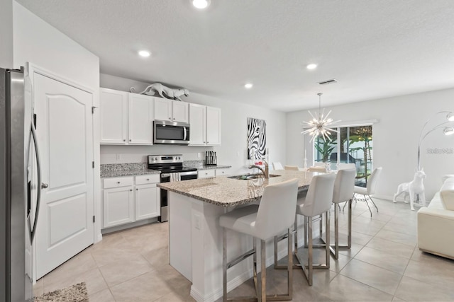 2355 White Lilly Dr, Kissimmee, FL 34747 - kitchen with stainless steel appliances, light stone counters, white cabinets, light tile patterned flooring, and a breakfast bar