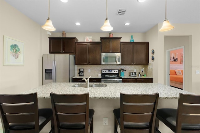 8912 Rhodes St, Kissimmee, FL 34747 - kitchen featuring stainless steel appliances, decorative backsplash, dark brown cabinetry, a kitchen island with sink, and decorative light fixtures