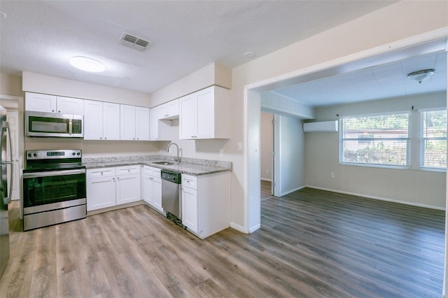 5908 Laconia Rd, Orlando, FL 32808 - kitchen with appliances with stainless steel finishes, light wood finished floors, light stone counters, white cabinets, and an AC wall unit
