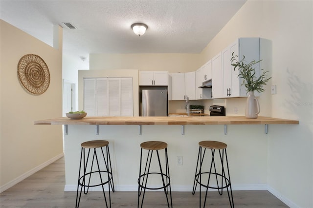 1065 Universal Rest Pl, Kissimmee, FL 34744 - kitchen with wood counters, refrigerator, a kitchen bar, a peninsula, and white cabinetry