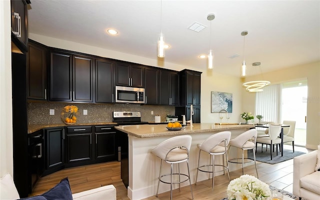 1222 Castlevecchio Loop, Orlando, FL 32825 - kitchen with appliances with stainless steel finishes, light wood-style flooring, decorative backsplash, a breakfast bar area, and pendant lighting