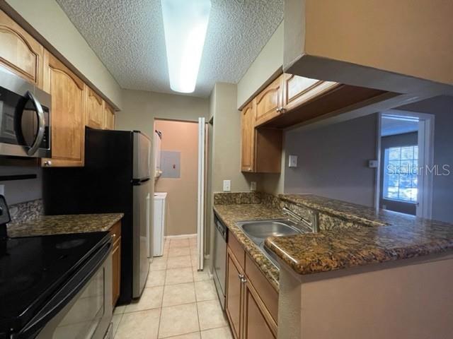236 Afton Sq Unit 207, Altamonte Springs, FL 32714 - kitchen featuring appliances with stainless steel finishes, a textured ceiling, light tile patterned floors, a peninsula, and dark stone counters