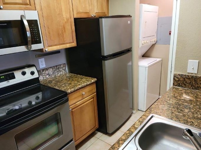 236 Afton Sq Unit 207, Altamonte Springs, FL 32714 - kitchen with stainless steel appliances, stacked washing machine and dryer, light tile patterned floors, and brown cabinetry