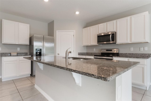 6808 Cranes Roost Rd, Harmony, FL 34773 - kitchen featuring appliances with stainless steel finishes, light tile patterned floors, an island with sink, dark stone countertops, and white cabinetry
