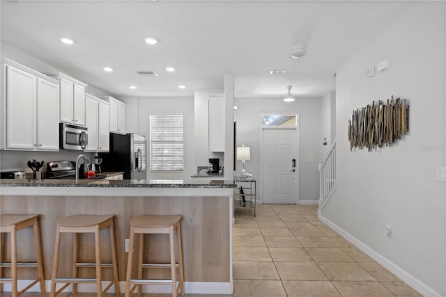 9023 Shadow Mountain St, Davenport, FL 33896 - kitchen featuring stainless steel appliances, a peninsula, dark stone counters, a kitchen bar, and white cabinets
