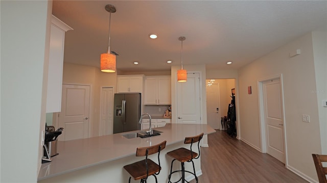 4858 Magnetite Loop, Mount Dora, FL 32757 - kitchen with stainless steel fridge with ice dispenser, a peninsula, white cabinets, wood finished floors, and a breakfast bar