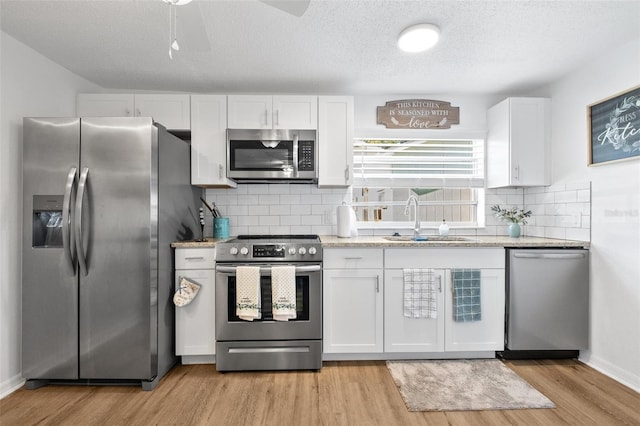 5141 Mallet Dr, Port Richey, FL 34668 - kitchen with stainless steel appliances, white cabinets, light wood-style floors, backsplash, and light stone counters