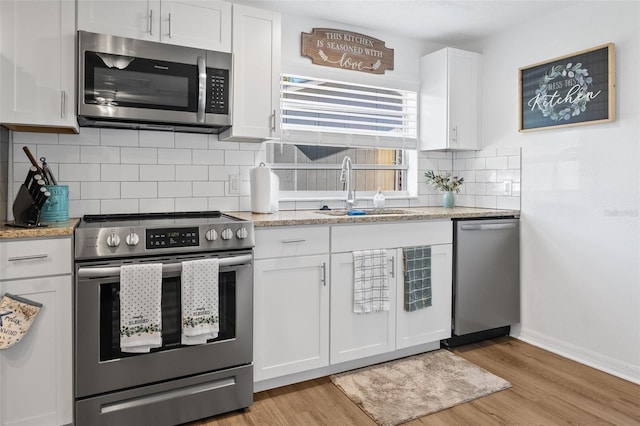 5141 Mallet Dr, Port Richey, FL 34668 - kitchen featuring stainless steel appliances, white cabinetry, light wood-type flooring, and tasteful backsplash