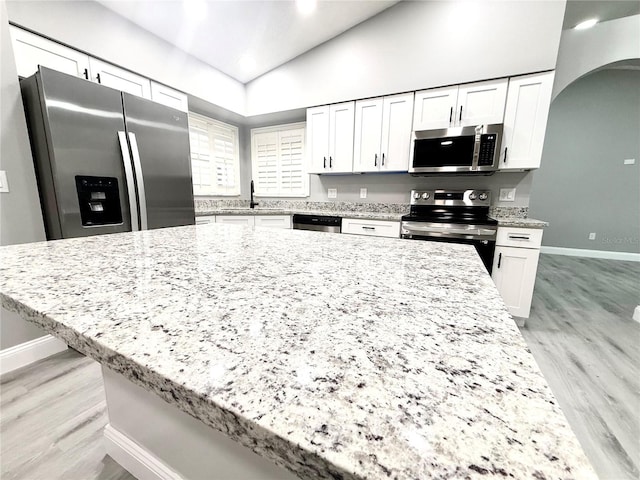 926 Freshmeadow Ct, Apopka, FL 32703 - kitchen with appliances with stainless steel finishes, light wood-style flooring, arched walkways, white cabinetry, and vaulted ceiling