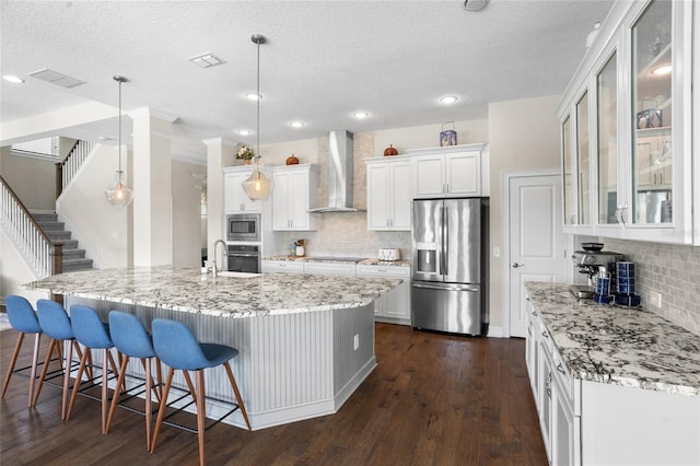 16412 Good Hearth Blvd, Clermont, FL 34711 - kitchen featuring stainless steel appliances, wall chimney range hood, decorative backsplash, white cabinets, and a kitchen breakfast bar