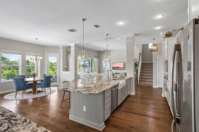 16412 Good Hearth Blvd, Clermont, FL 34711 - kitchen with appliances with stainless steel finishes, a chandelier, dark wood-style flooring, decorative columns, and light stone counters