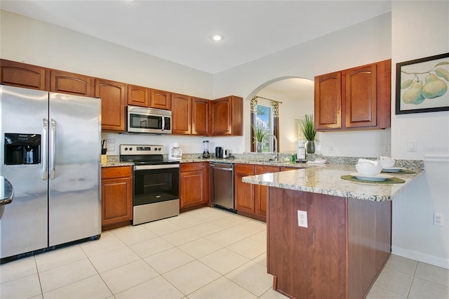 2669 Manesty Ln, Kissimmee, FL 34747 - kitchen with stainless steel appliances, arched walkways, a peninsula, light tile patterned floors, and brown cabinets
