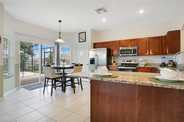 2669 Manesty Ln, Kissimmee, FL 34747 - kitchen featuring appliances with stainless steel finishes, light stone counters, a peninsula, decorative light fixtures, and brown cabinets