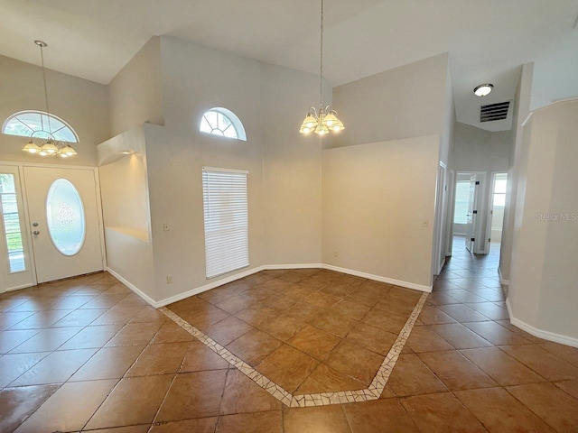 foyer entrance with a chandelier, a towering ceiling, plenty of natural light, tile patterned floors, and inlaid floor details