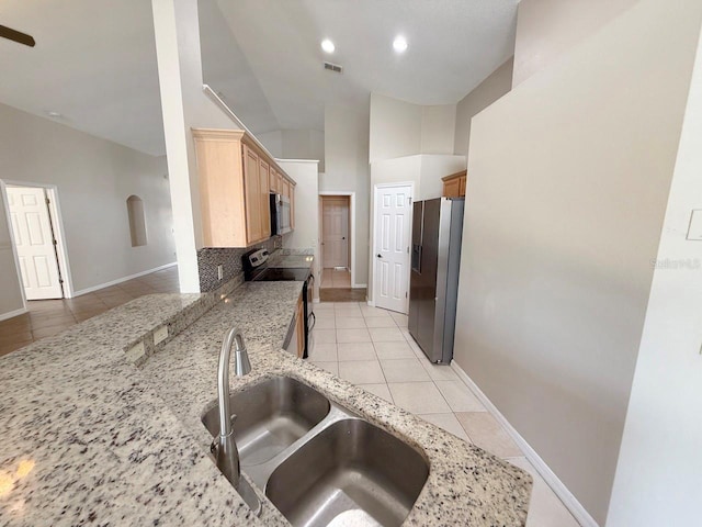 kitchen with appliances with stainless steel finishes, light tile patterned floors, lofted ceiling, tasteful backsplash, and light stone countertops